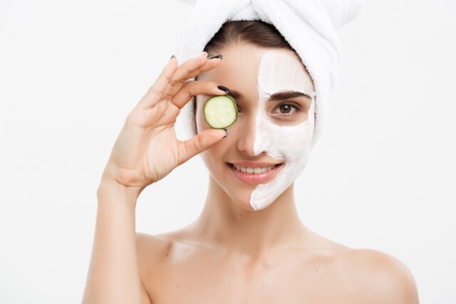 Beauty Youth Skin Care Concept - Portrait Beautiful Caucasian Woman apply cream and holding fresh cucumber in front of her face.Isolated over white background.